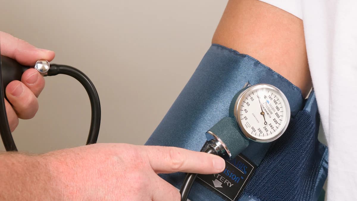 A pharmacist taking a patient's blood pressure reading using an automated cuff in a pharmacy consultation room