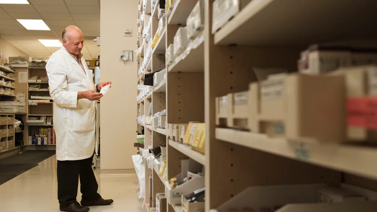 A pharmacist in a white coat standing beside a well-stocked medicine shelf in a community pharmacy