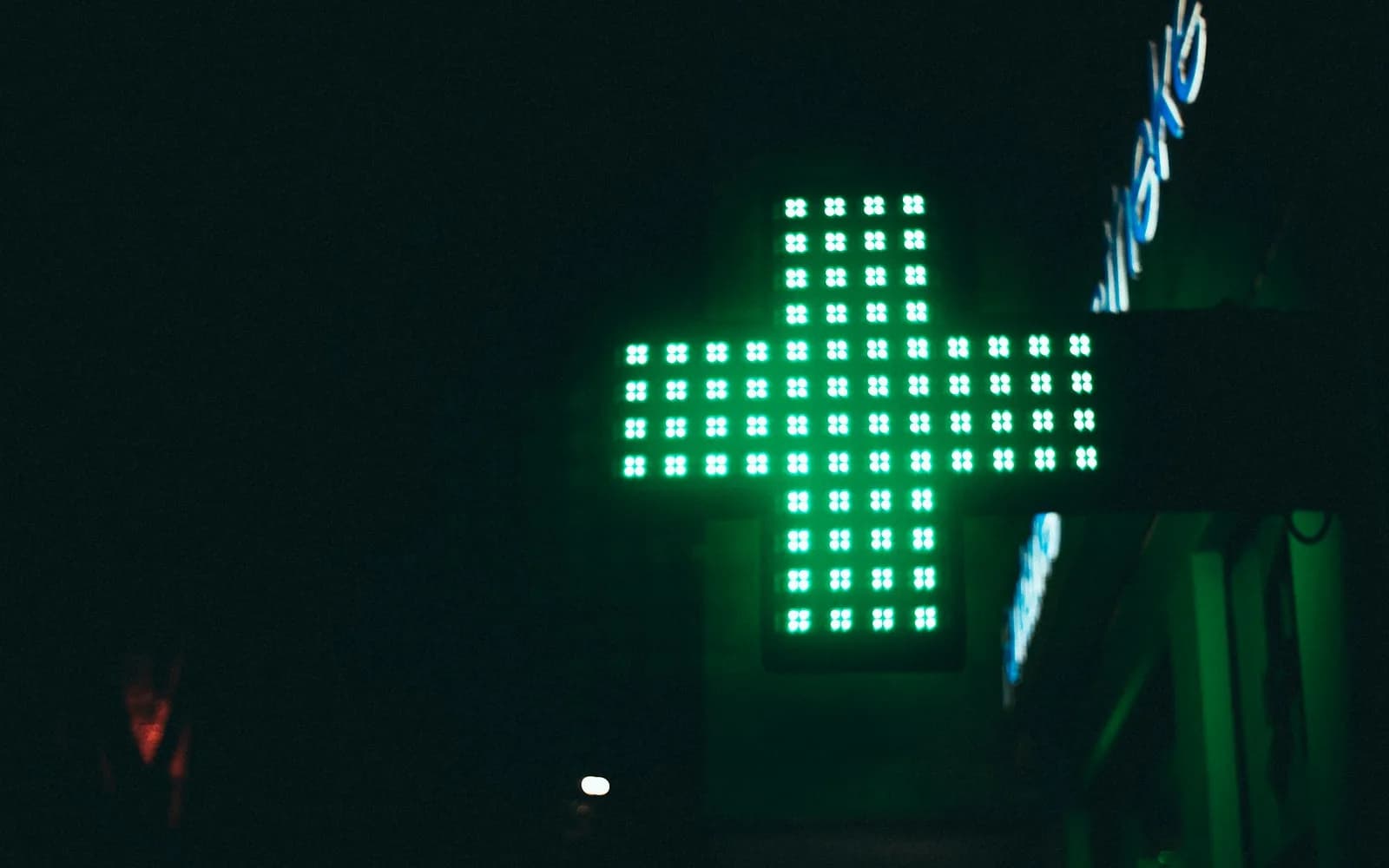 A green illuminated pharmacy cross sign at night